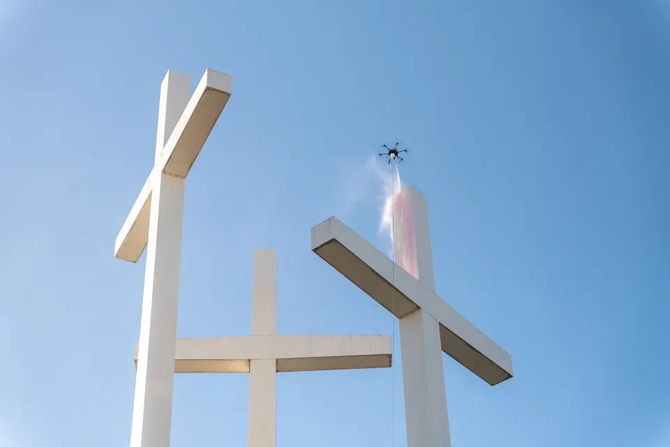 Cleaning drone soft washing large white cross sculptures at a church campus against a clear blue sky
