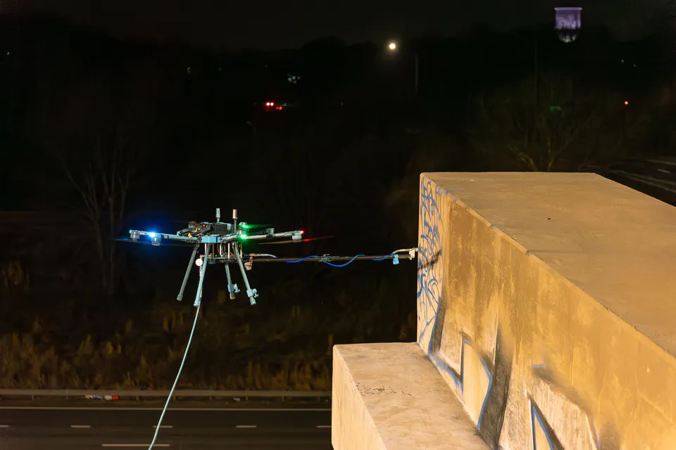 Lucid Bots Sherpa cleaning drone operating beside graffiti on a concrete overpass at night